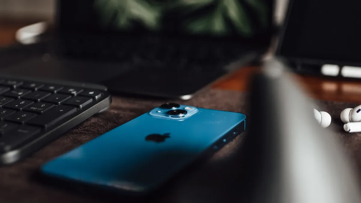 An iPhone, a keyboard, a laptop, and a pair of AirPods lying close together on a desk
